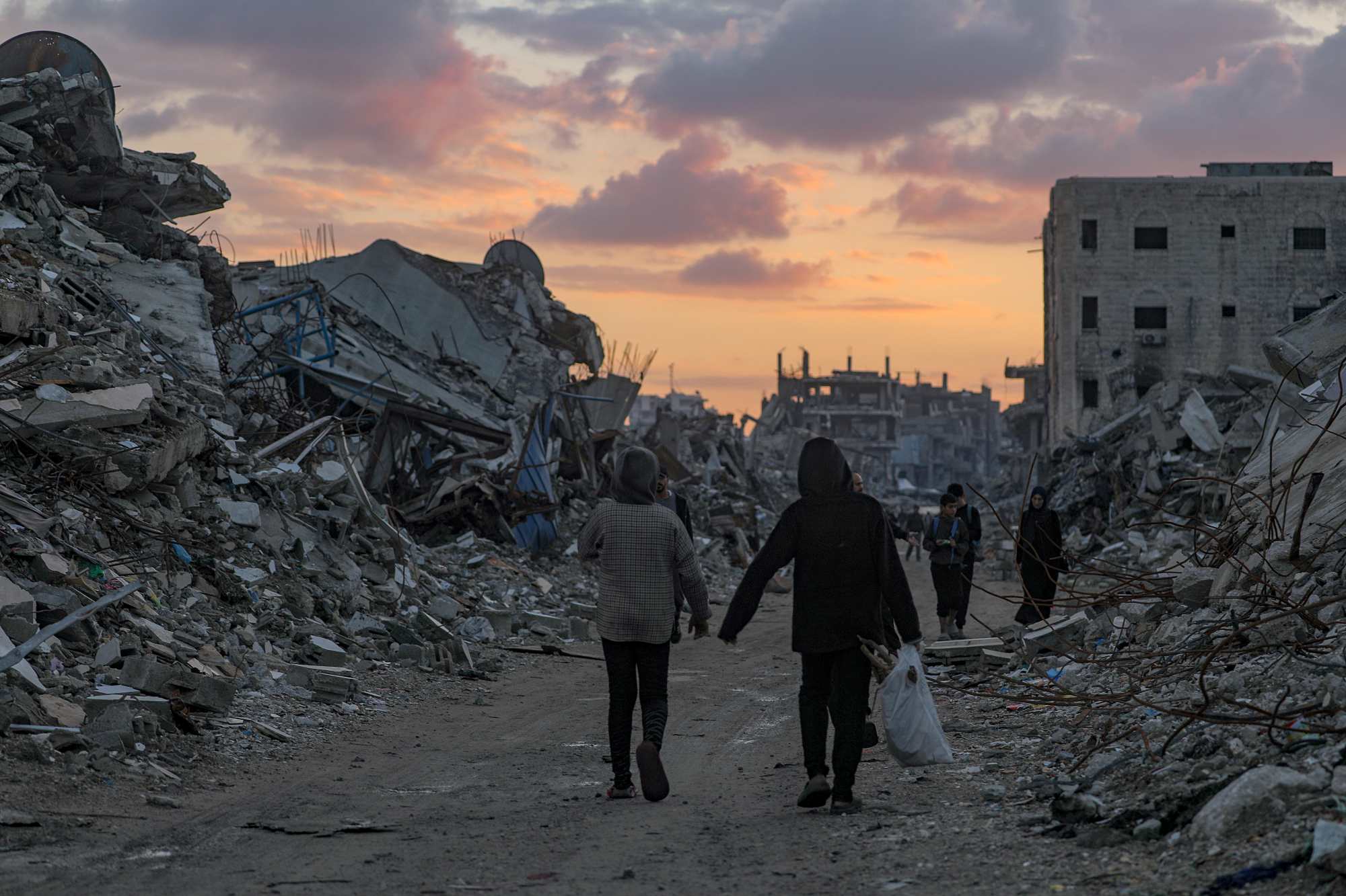 Palestinians walk near destroyed buildings on a rainy day in eastern Gaza City.