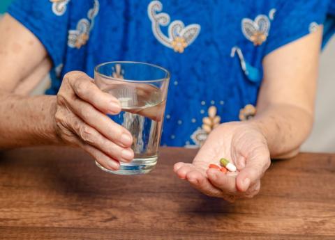 An older woman takes tablets with a glass of water.