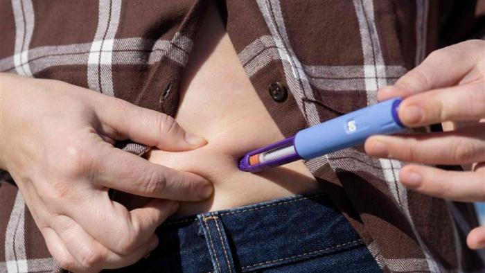 A person injecting medication into their abdomen.